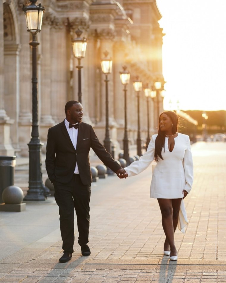 A couple walking at sunrise past the Louvre in Paris