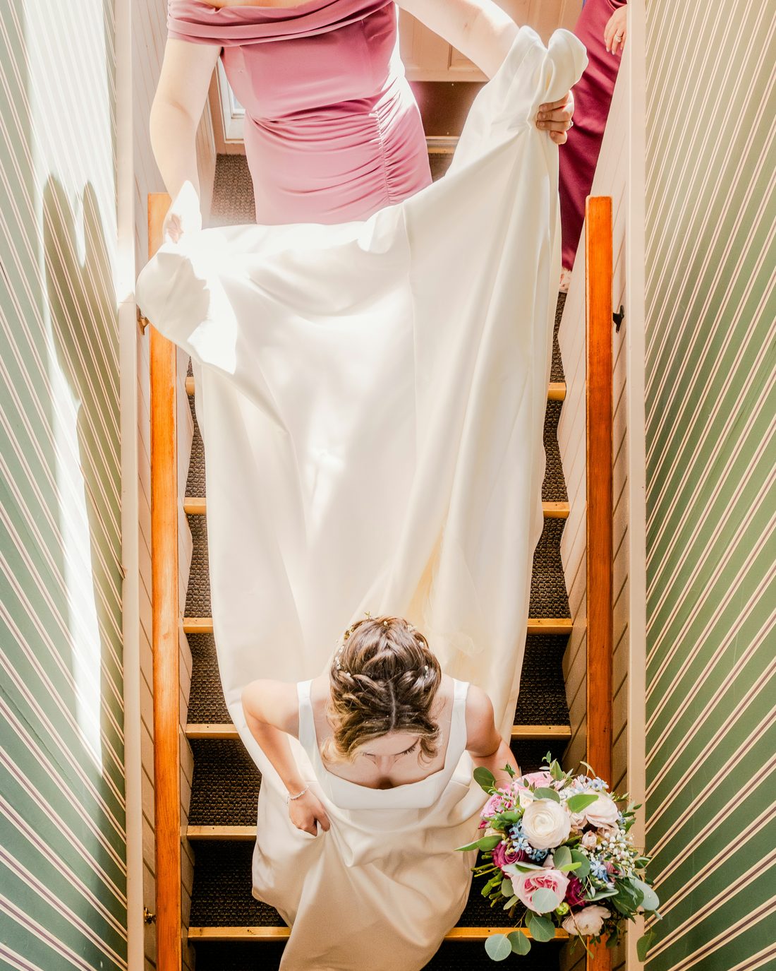 Bridesmaids carrying a bride's train down a staircase