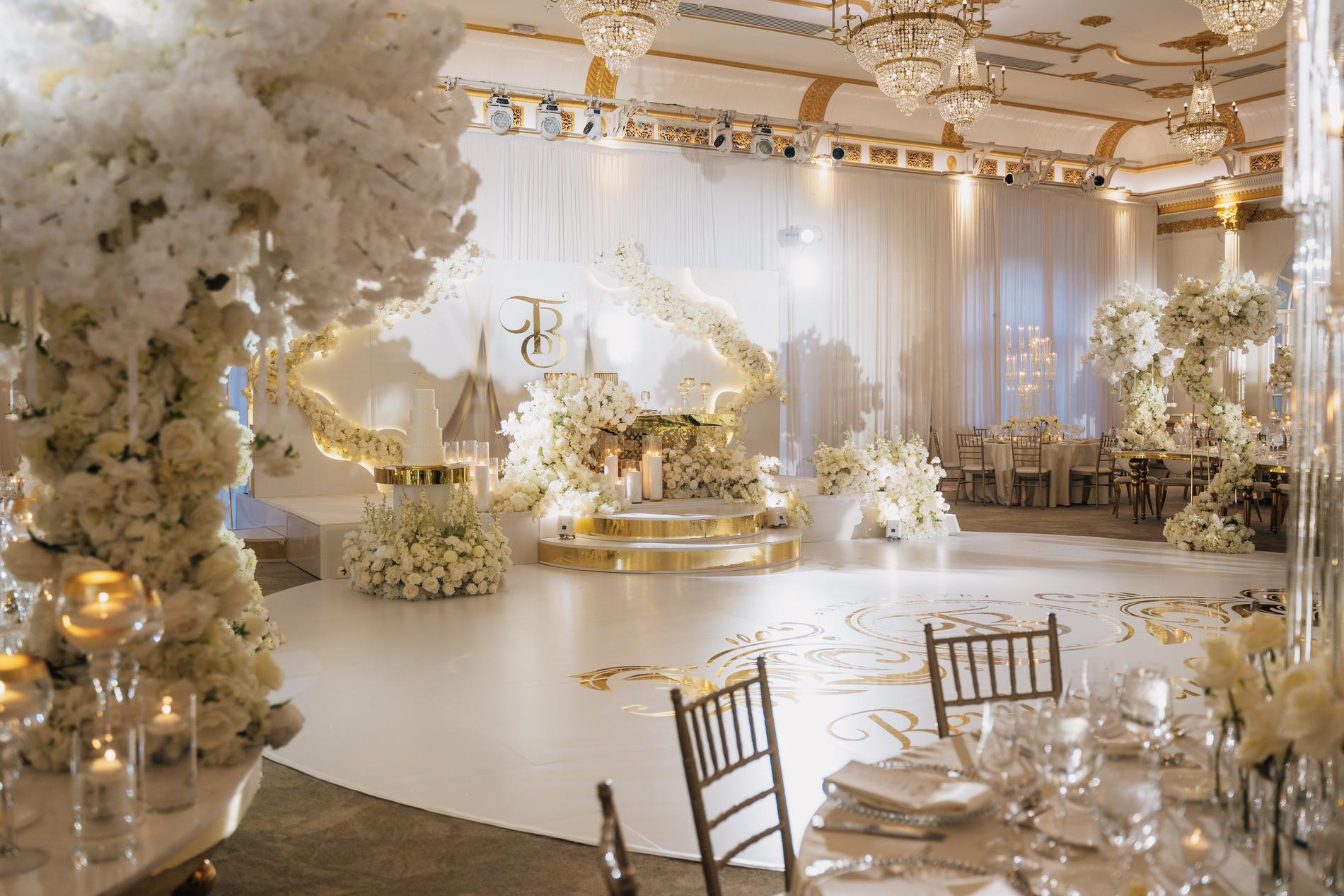 A ballroom set for the reception, gold dance floor and white florals, before the guests arrive