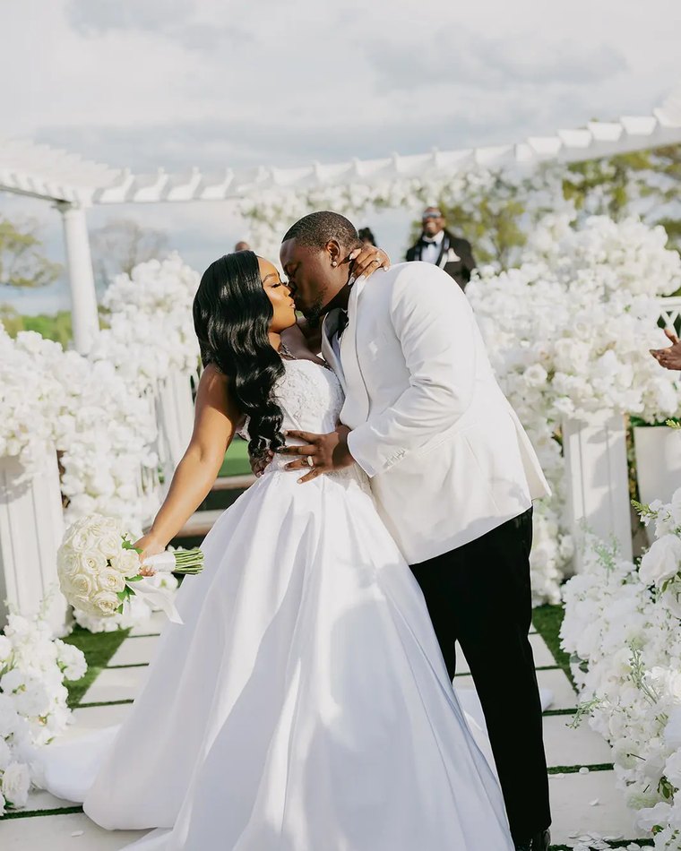 A couple kissing at their ceremony under a white floral arch