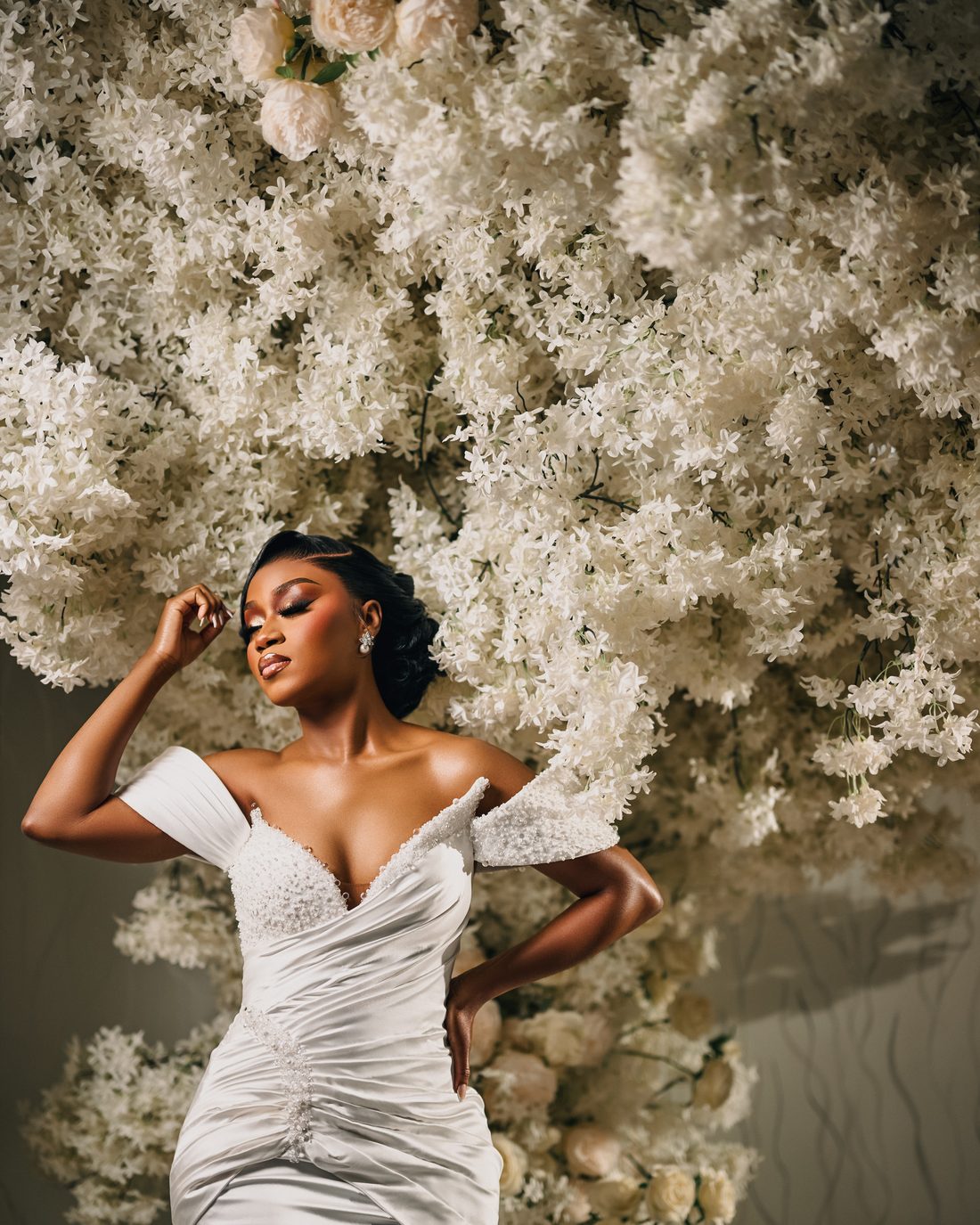 A bride in ivory satin against a wall of white blossom