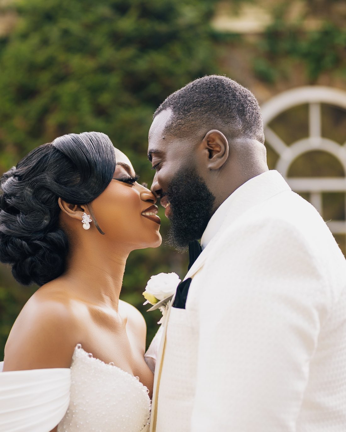 A bride and groom leaning in to kiss beside their car